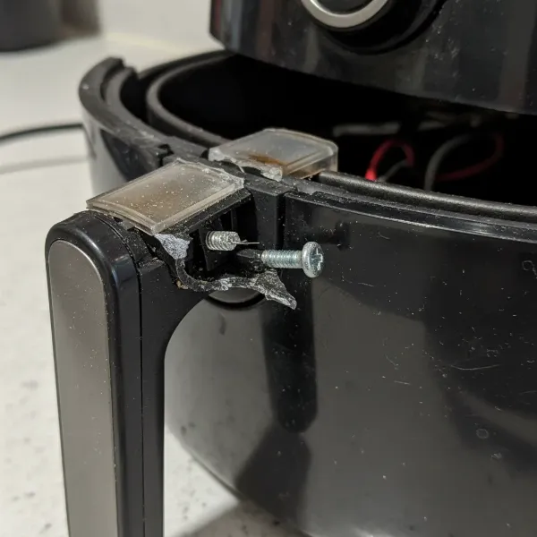 Close-up of a broken air fryer drawer handle, showing snapped plastic or loose screws, with a focus on the damage.